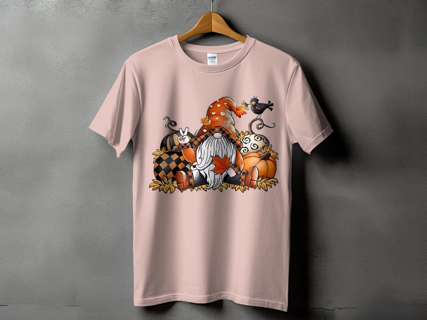 Gnome with pumpkins and a bird graphic on a light pink t-shirt.