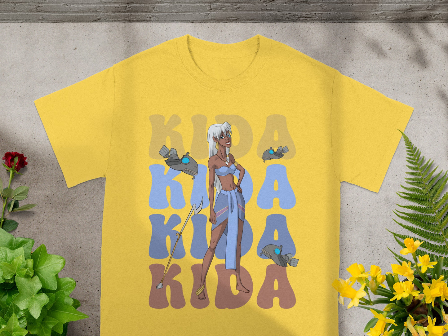 Kida in blue outfit with staff, on yellow t-shirt with blue text.