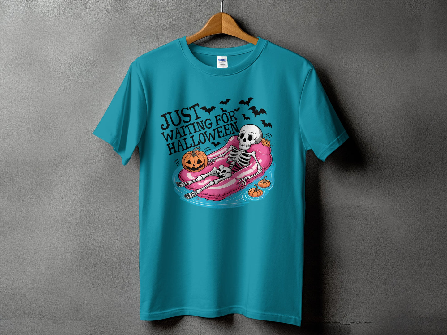 Teal t-shirt with skeleton on float, pumpkin, bats, and text "JUST WAITING FOR HALLOWEEN".
