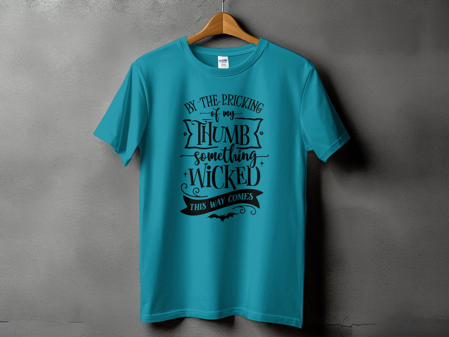 Teal t-shirt with black text: "By the pricking of my thumb something wicked this way comes."