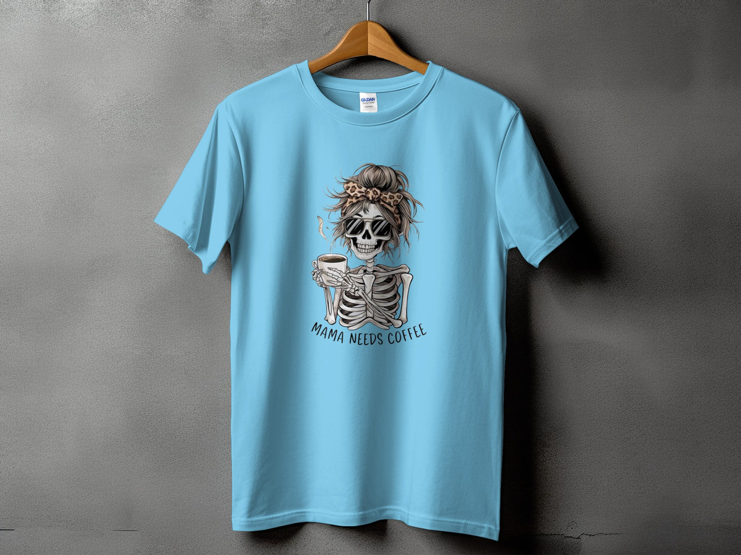Light blue t-shirt with a skeleton graphic drinking coffee, text "Mama Needs Coffee."