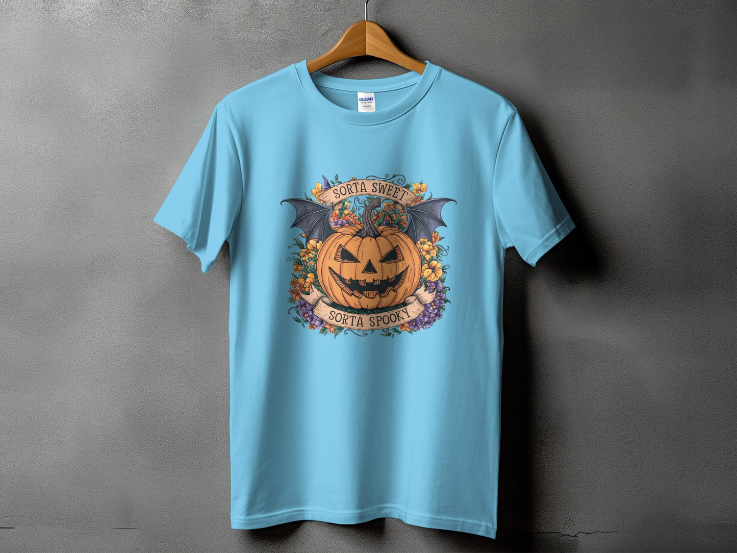 Light blue t-shirt with Halloween graphic of a pumpkin with bat wings, flowers, and text.