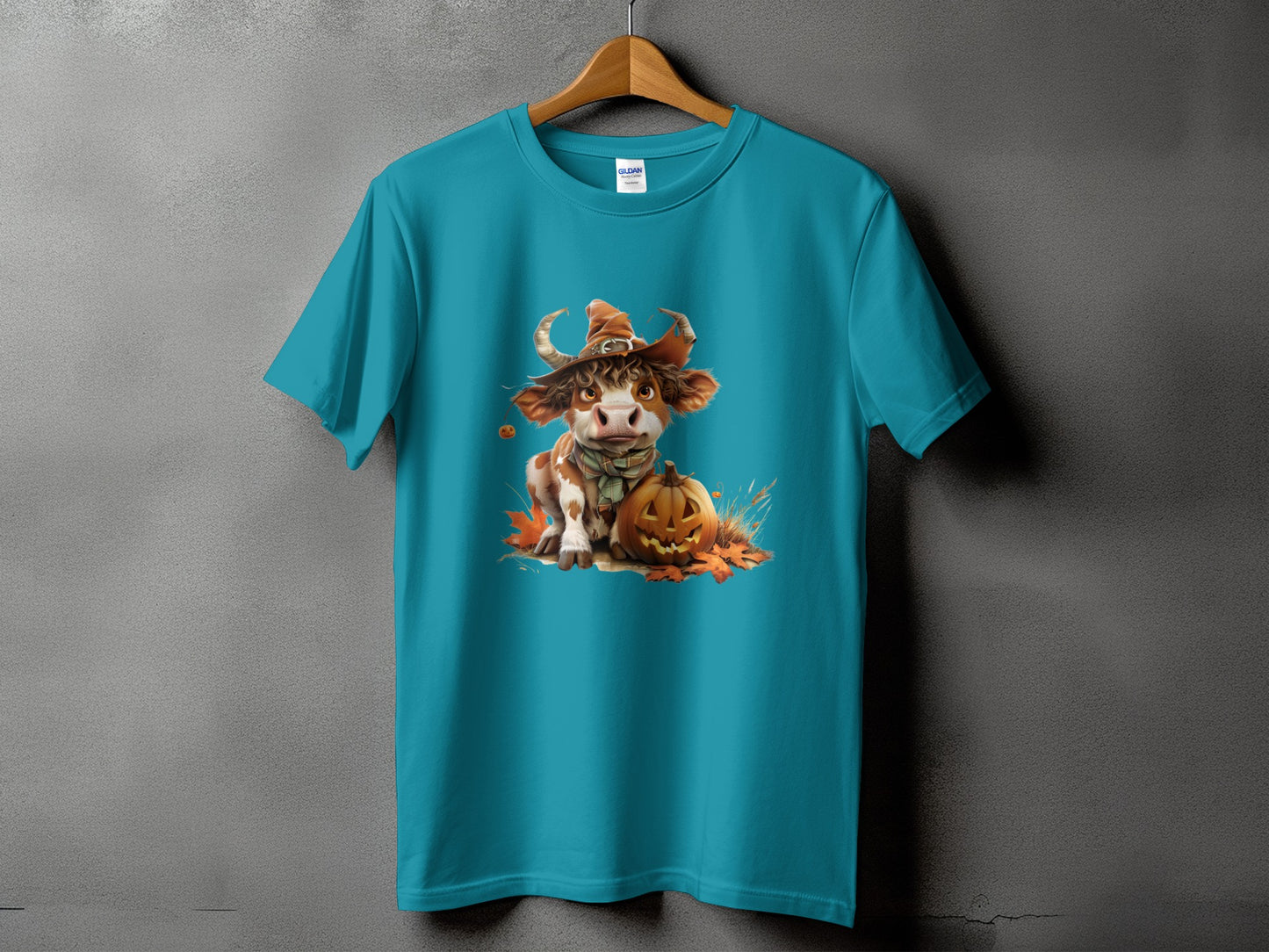 Teal t-shirt with a cow wearing a witch hat and holding a pumpkin.