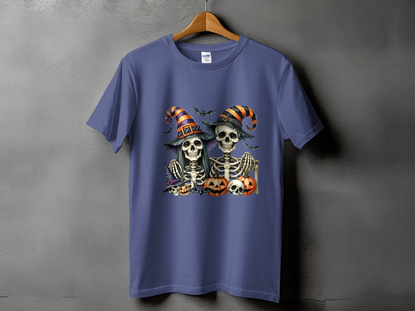 Two skeletons in witch hats with bats and pumpkins on a purple t-shirt.