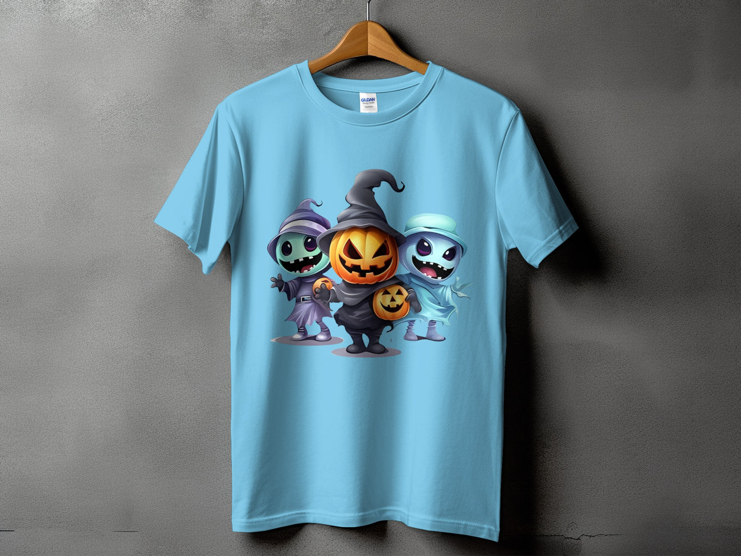 Light blue t-shirt with three cartoon Halloween characters: a witch, a pumpkin, and a ghost.