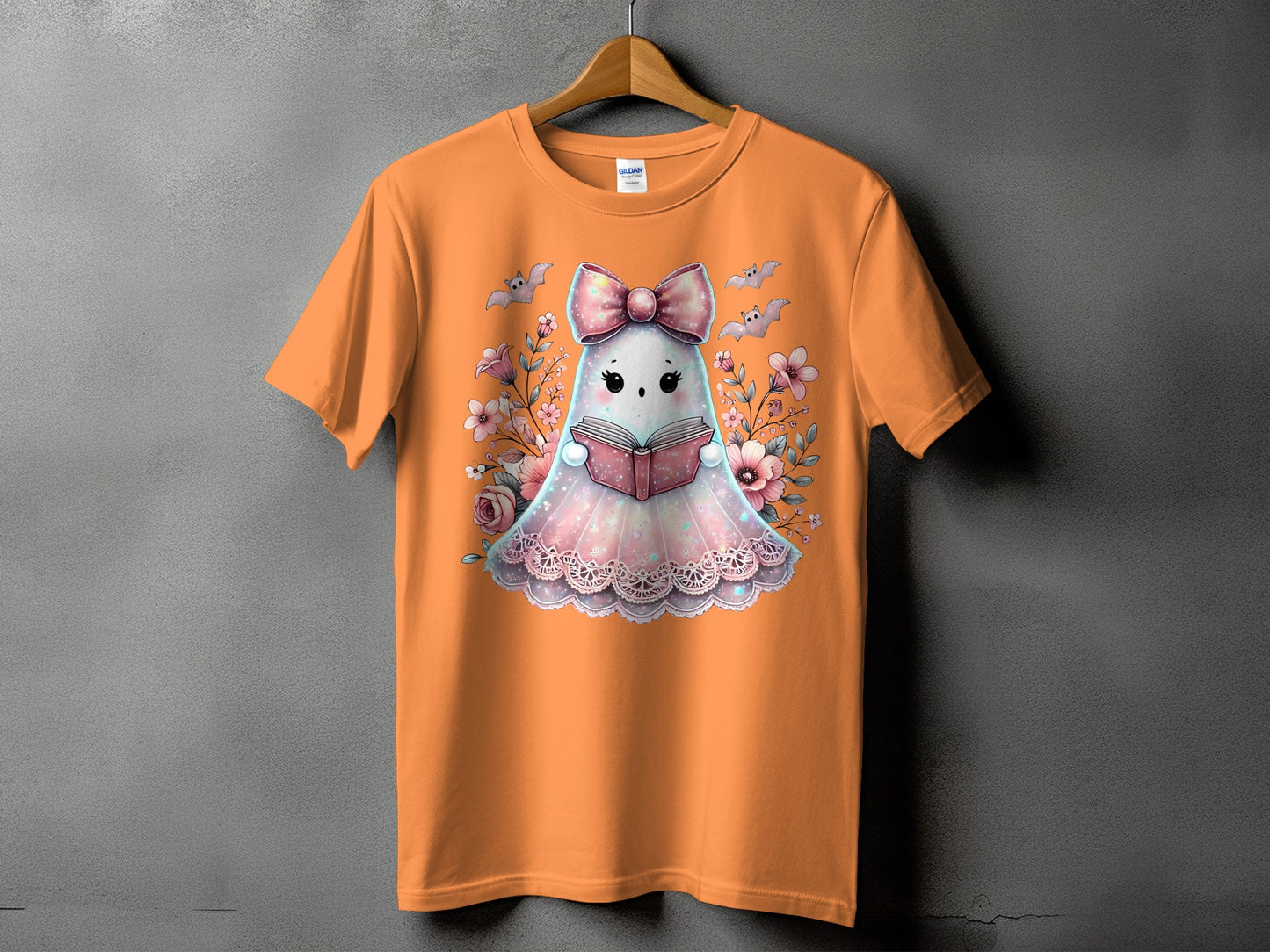Orange t-shirt with a cute ghost reading a book surrounded by flowers and bats.