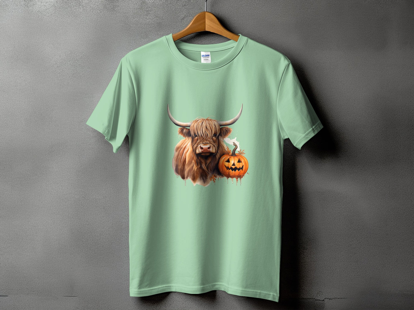 Highland cow with pumpkin graphic on mint green t-shirt.