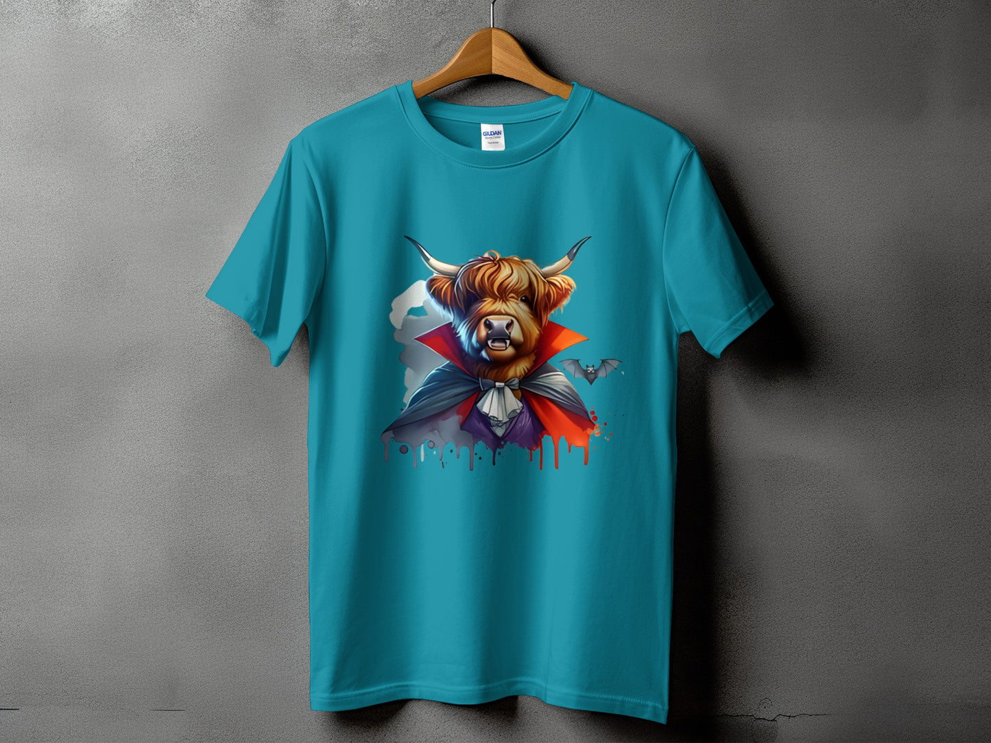 Highland cow dressed as a vampire with bats, printed on a teal t-shirt.