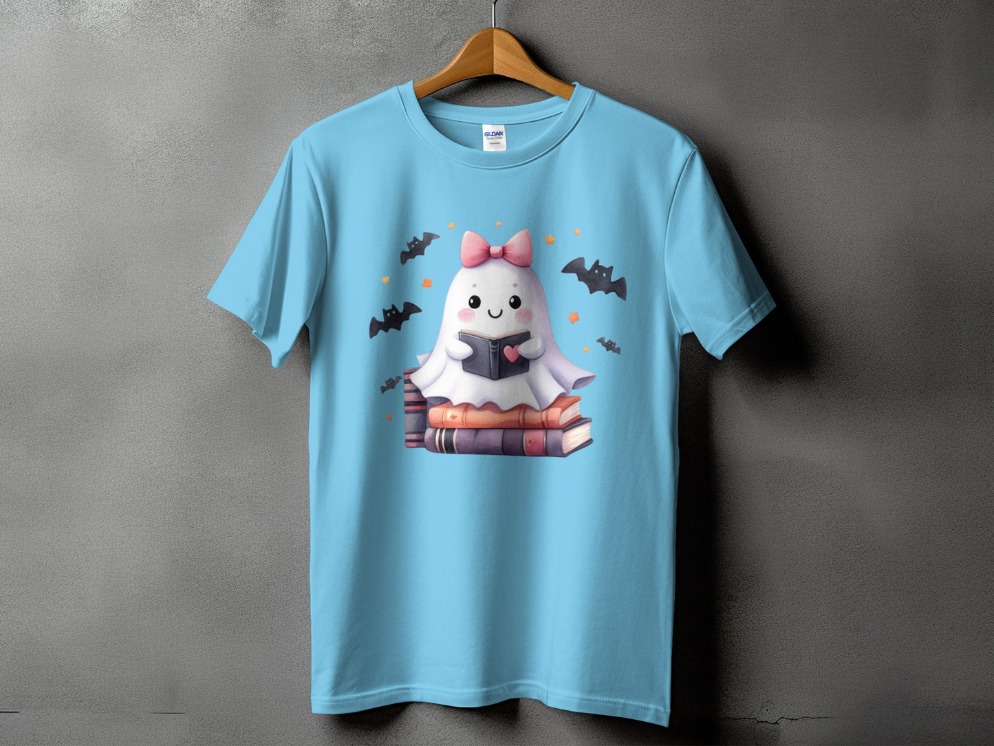 Light blue t-shirt with a cute ghost reading a book on a stack of books.