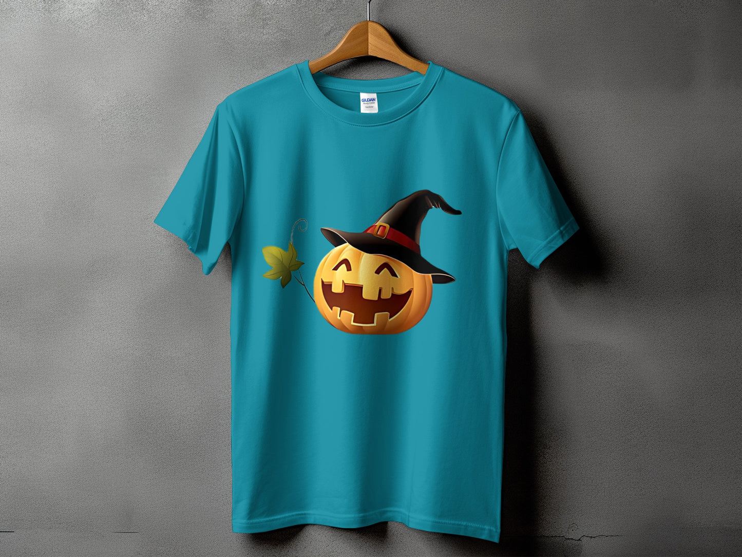 Teal t-shirt with a smiling jack-o'-lantern wearing a witch hat and a leaf.
