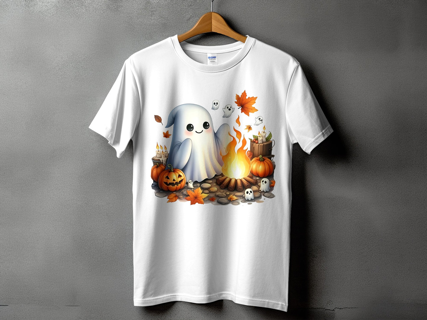 White t-shirt with a Halloween graphic of a ghost by a campfire with pumpkins and falling leaves.