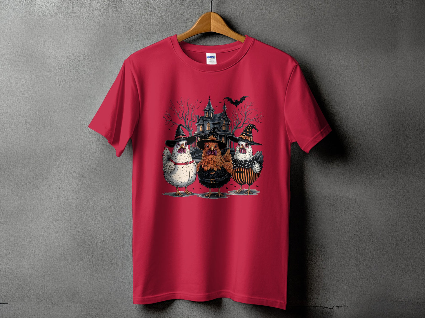 Red t-shirt with graphic of three chickens in witch hats in front of a haunted house.