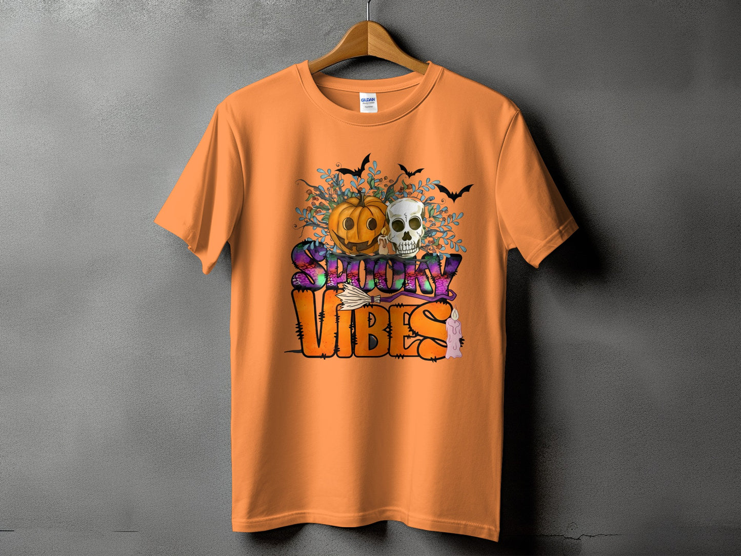 Orange t-shirt with Halloween graphic featuring a pumpkin, skull, bats, and text "Spooky Vibes".