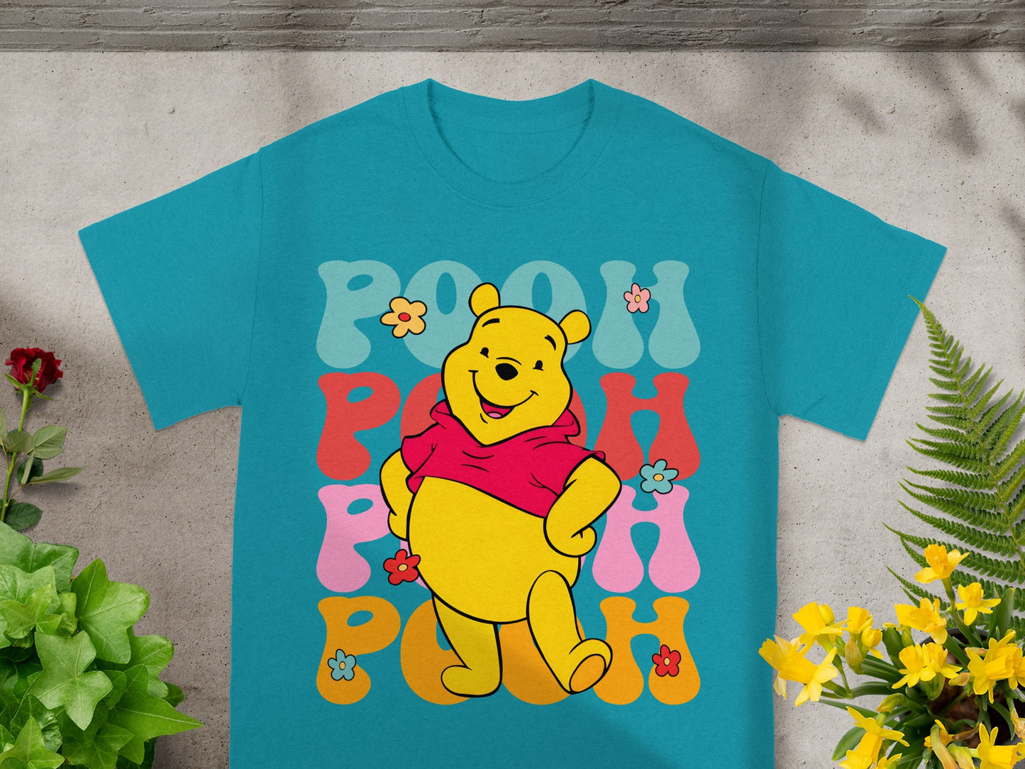 Winnie the Pooh and colorful text spelling "Pooh" on a turquoise t-shirt.
