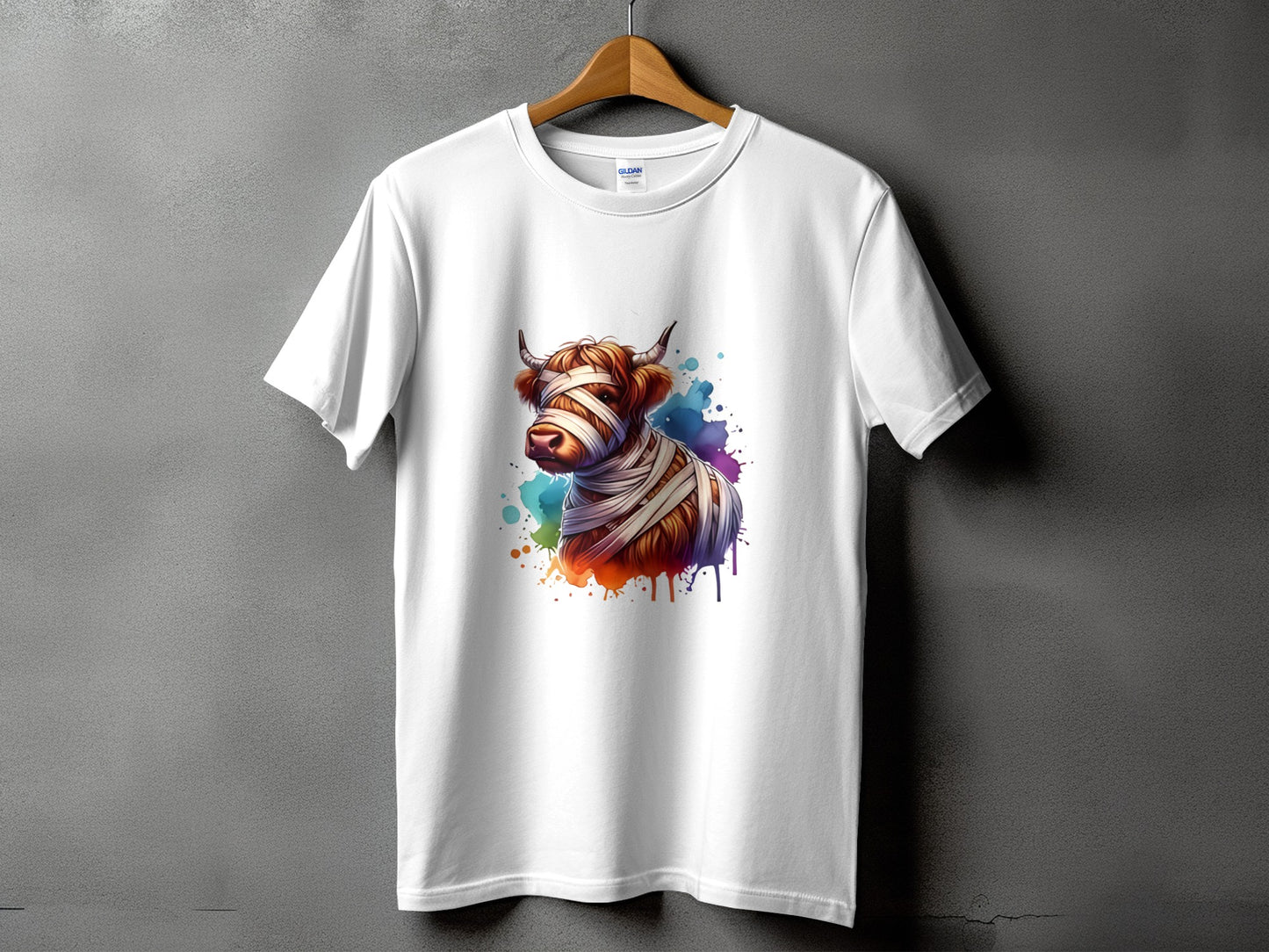 White t-shirt with a Highland cow wrapped in bandages and colorful paint splatters.