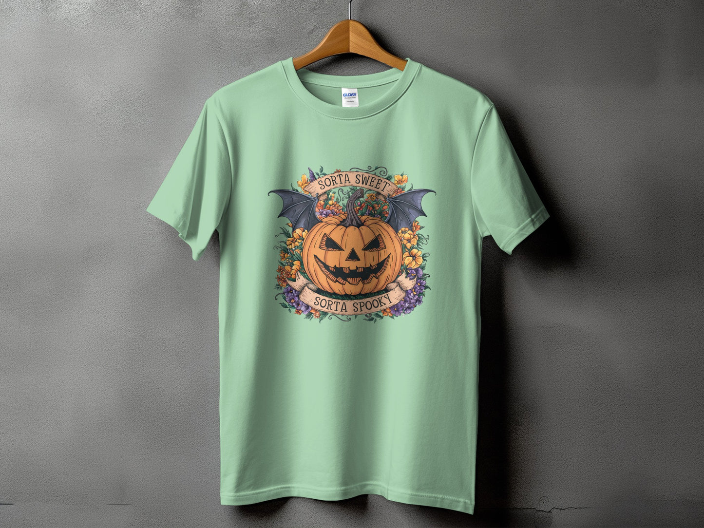 Green t-shirt with a Halloween design featuring a jack-o'-lantern, bat wings, and floral accents.