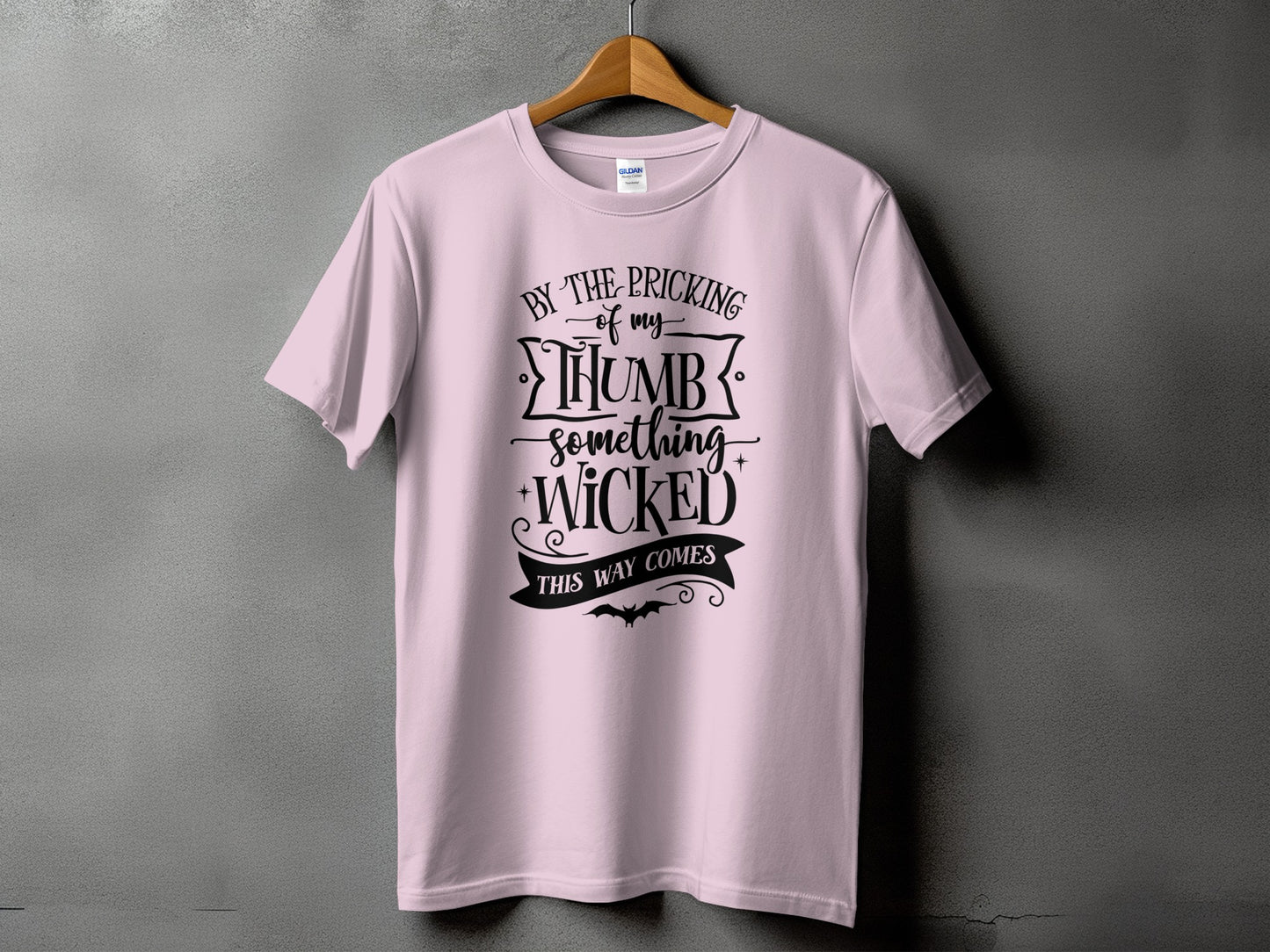 Light pink t-shirt with black text "By the pricking of my thumb something wicked this way comes".