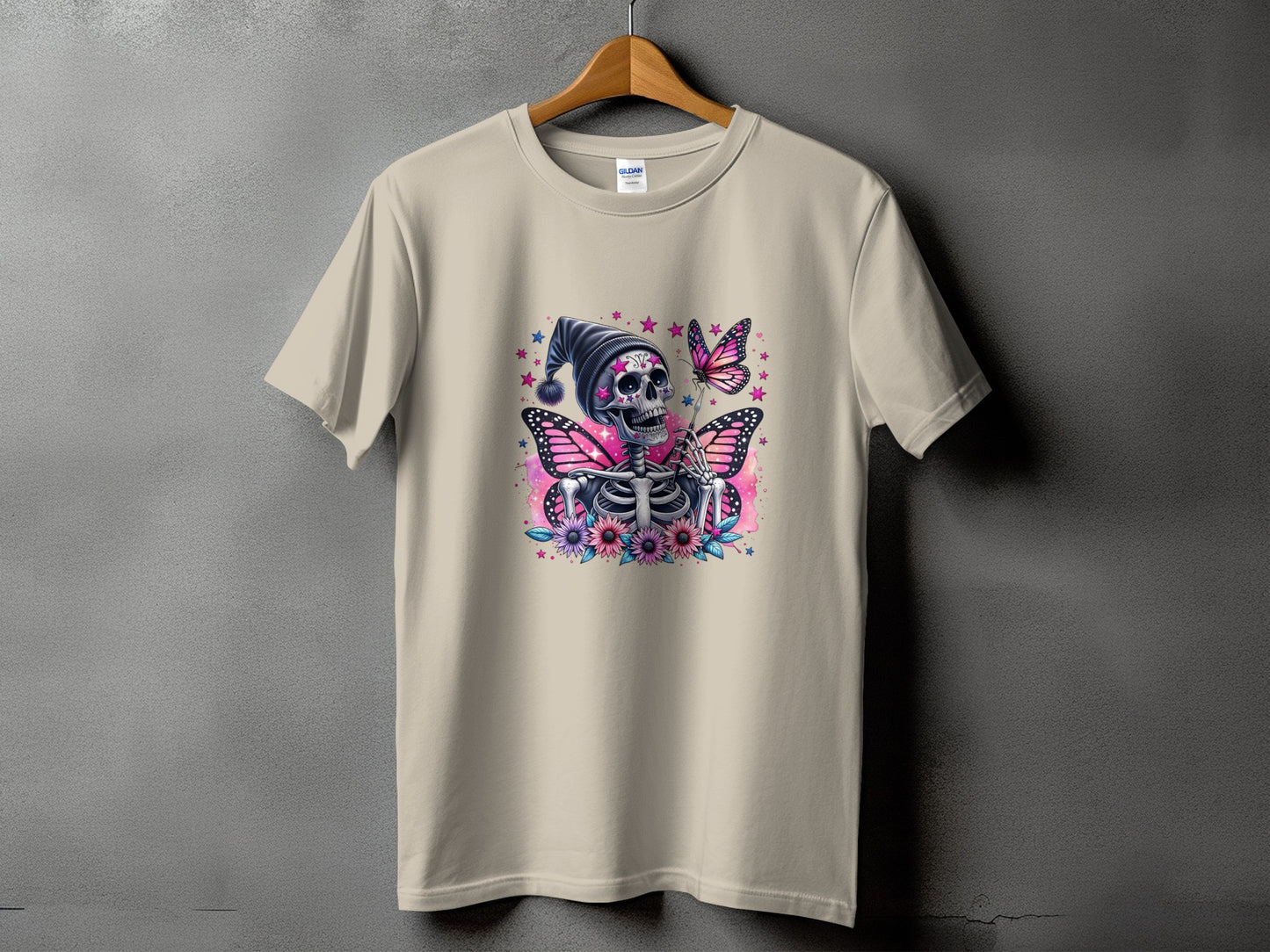 Skeleton with butterfly wings, flowers, and stars graphic on a light tan t-shirt.