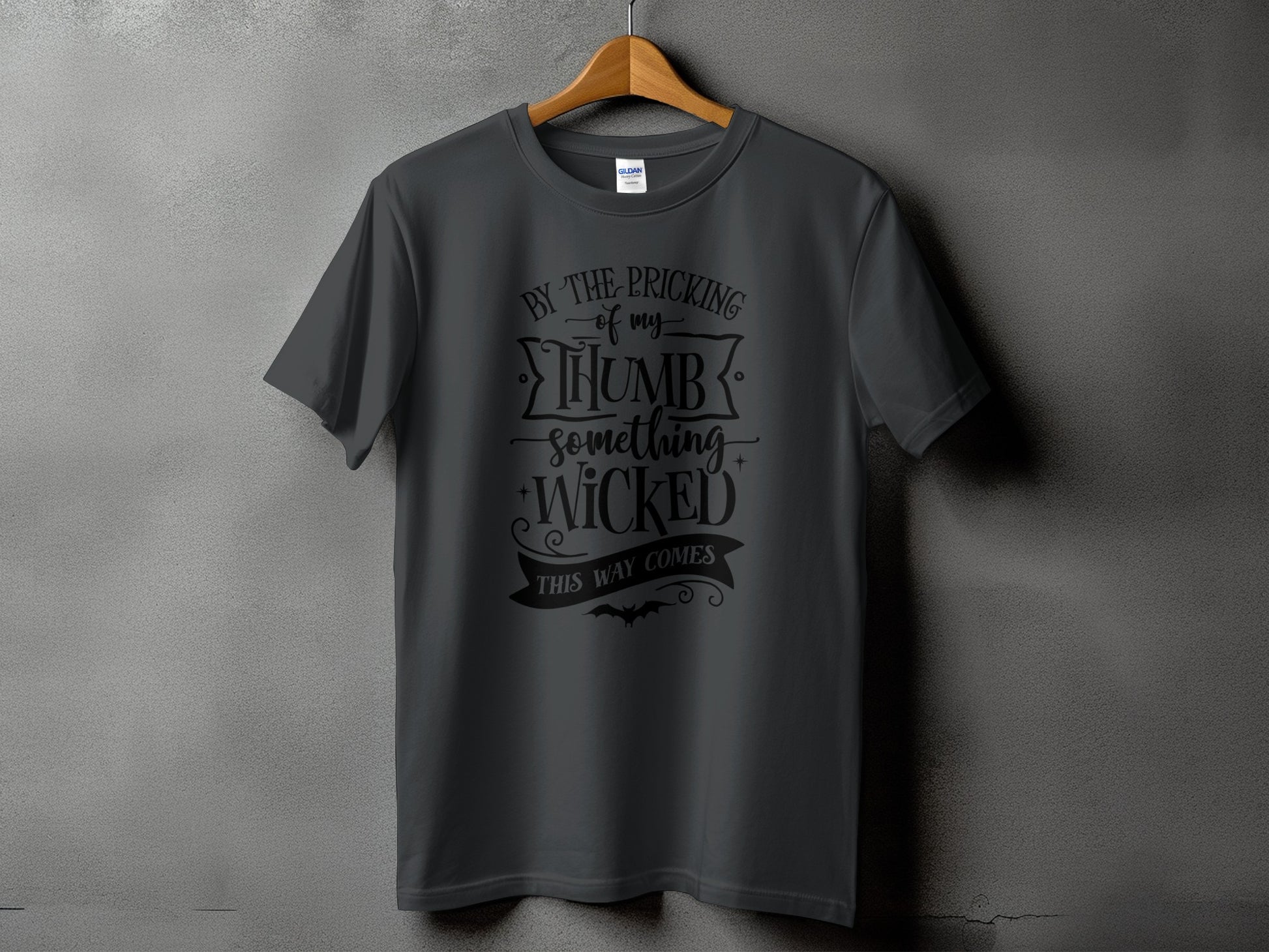 Dark gray t-shirt with black text: "By the pricking of my thumb, something wicked this way comes"