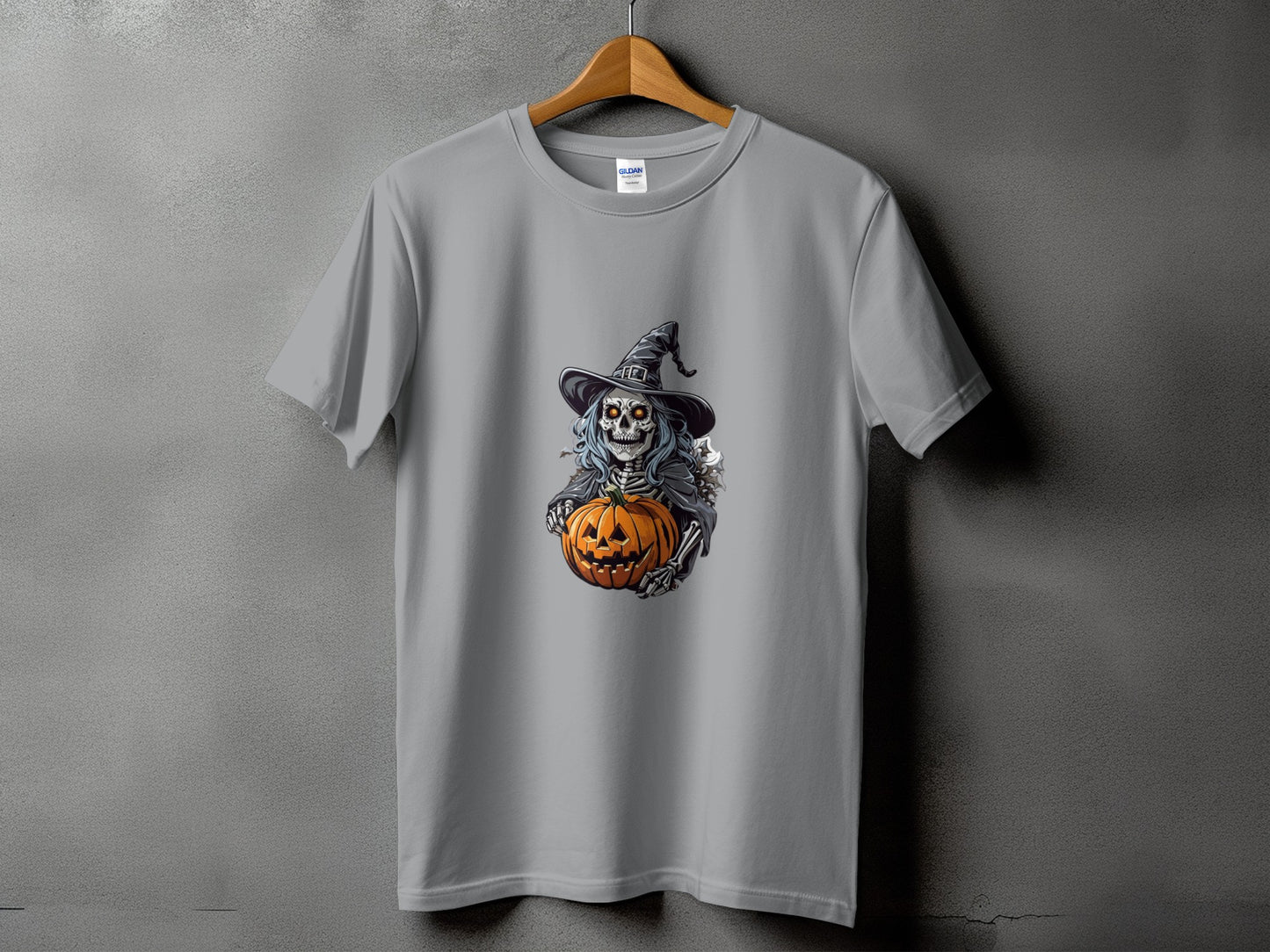 Skeleton in witch hat holds carved pumpkin on grey t-shirt.