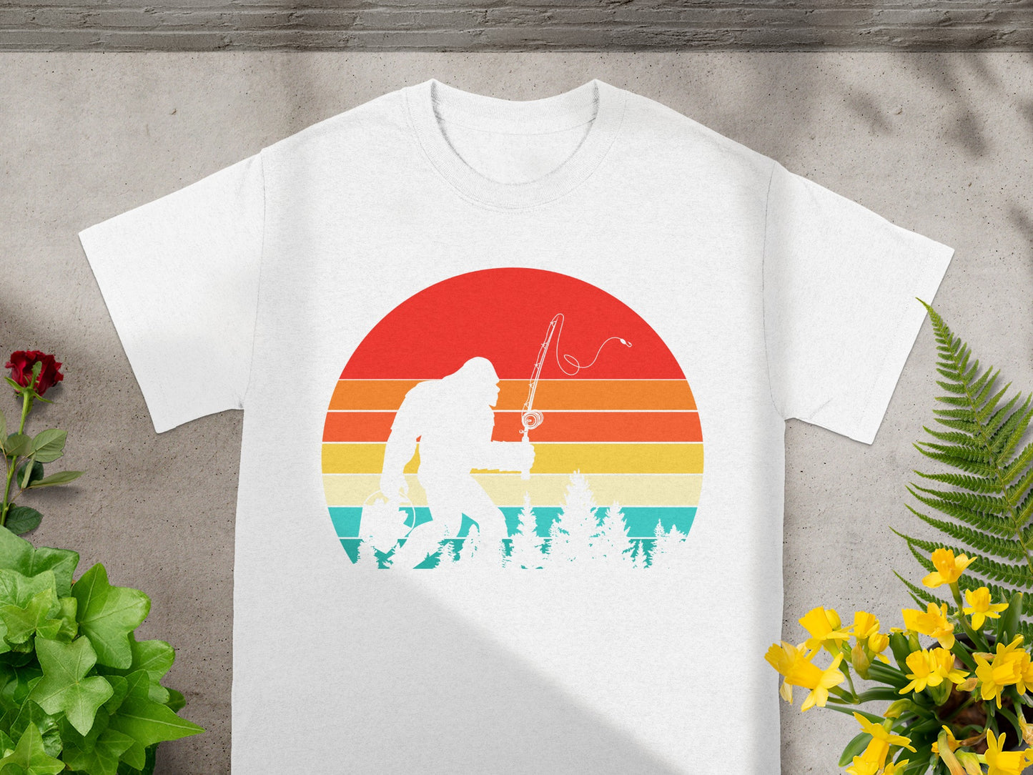 White t-shirt with Bigfoot fishing in front of a retro sunset graphic.