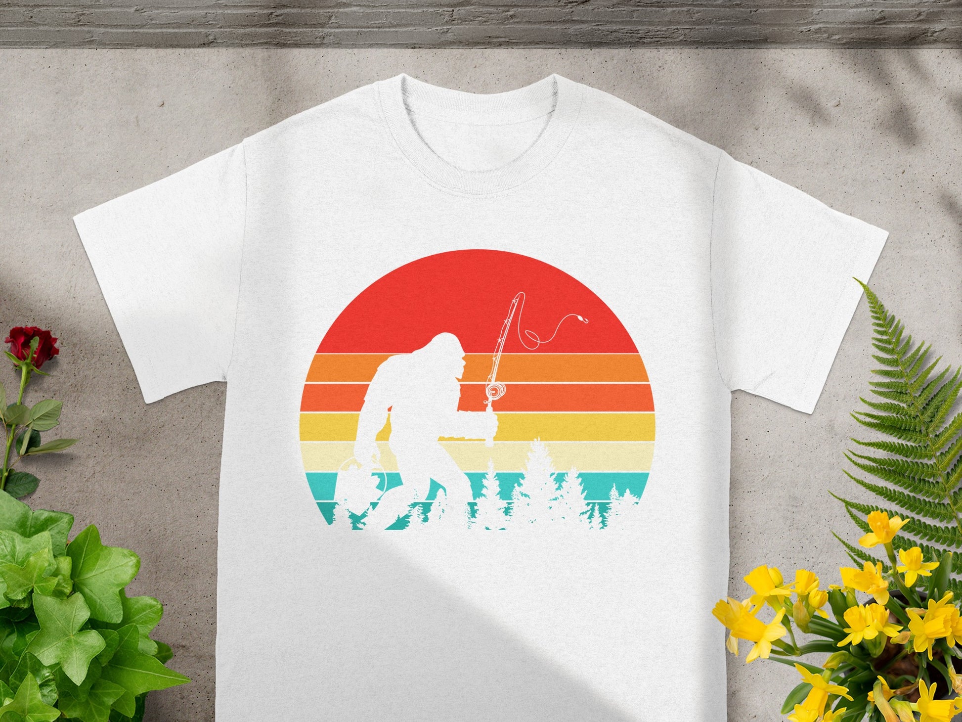 White t-shirt with Bigfoot fishing in front of a retro sunset graphic.