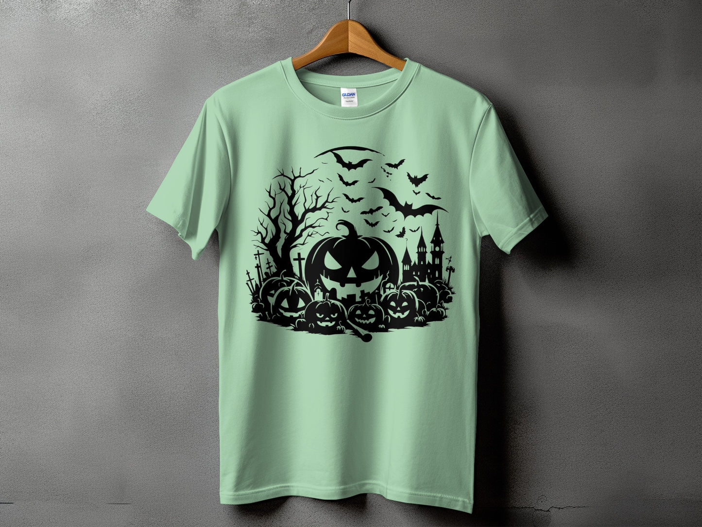 Black Halloween graphic with pumpkins, bats, and a haunted castle on a light green t-shirt.