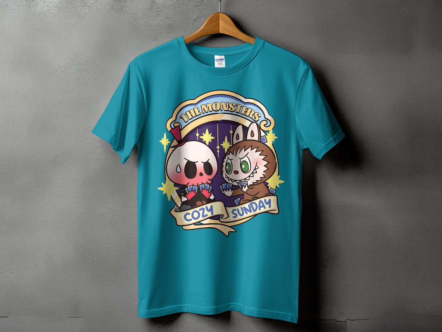 Teal t-shirt with "The Monsters Cozy Sunday" graphic of two cartoon monsters playing cards.