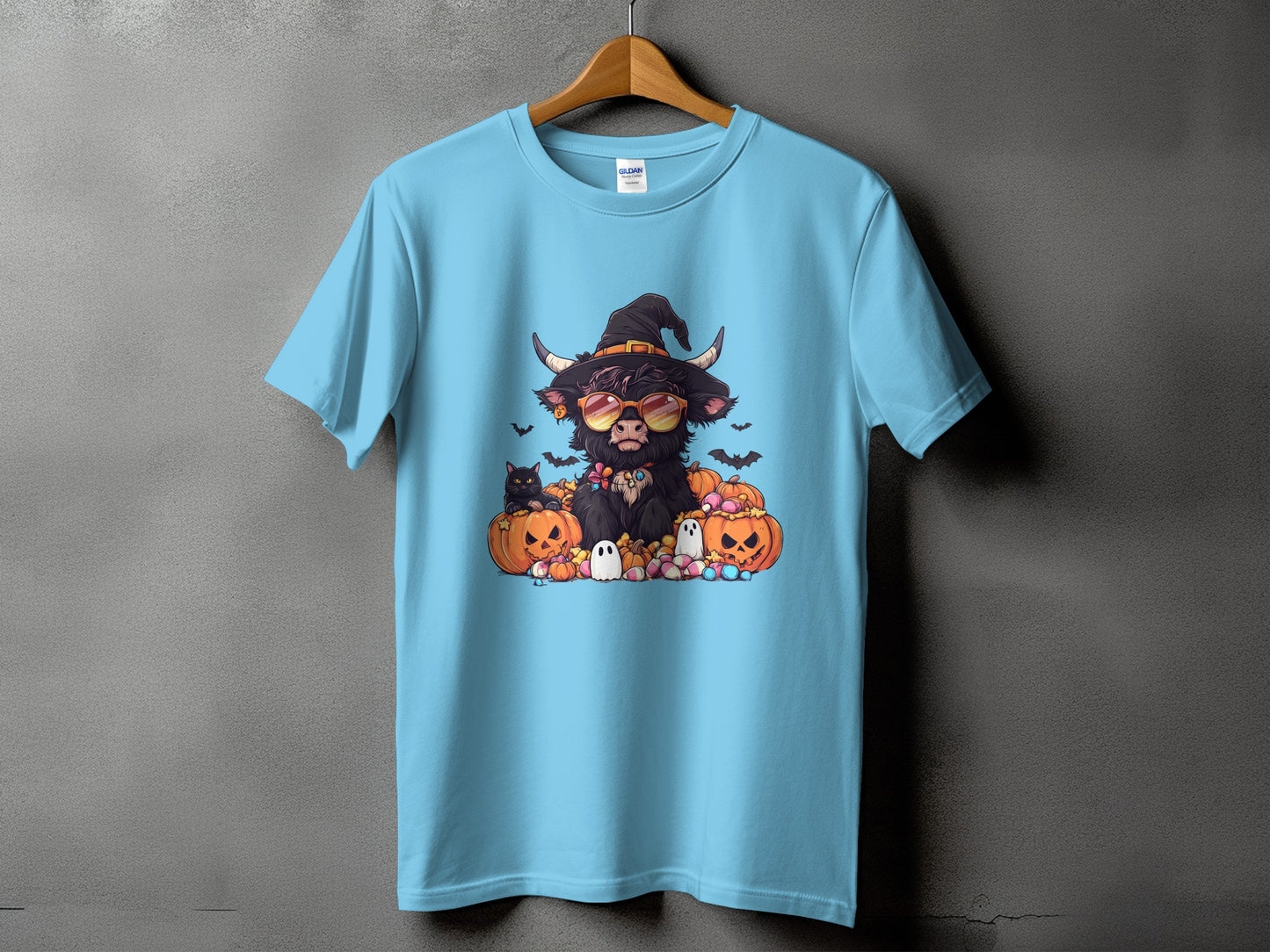 T-shirt with a cartoon highland cow wearing a witch hat, sunglasses, and surrounded by pumpkins.