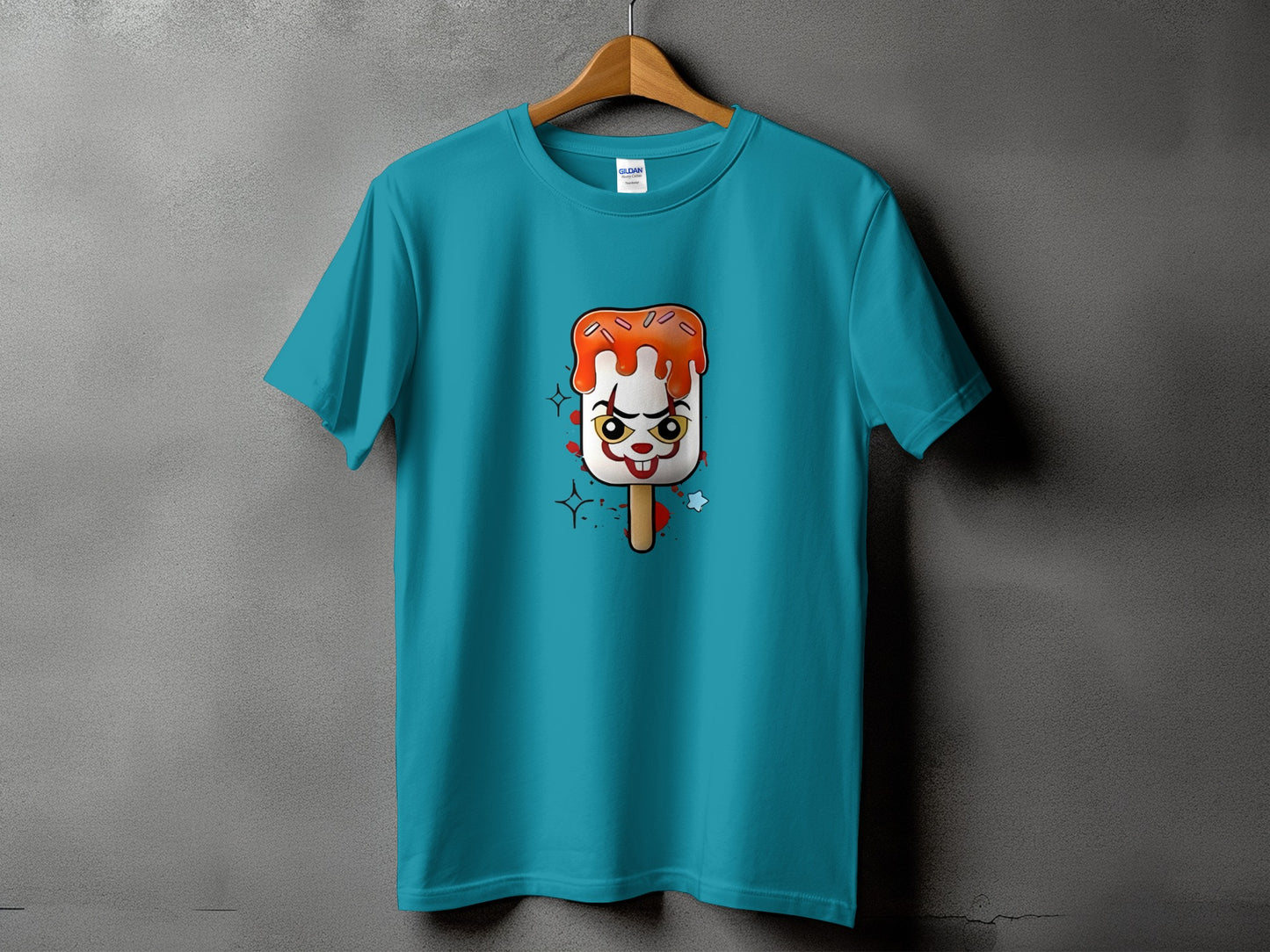 Teal t-shirt with a clown-faced popsicle graphic wearing an orange icing and brown stick.