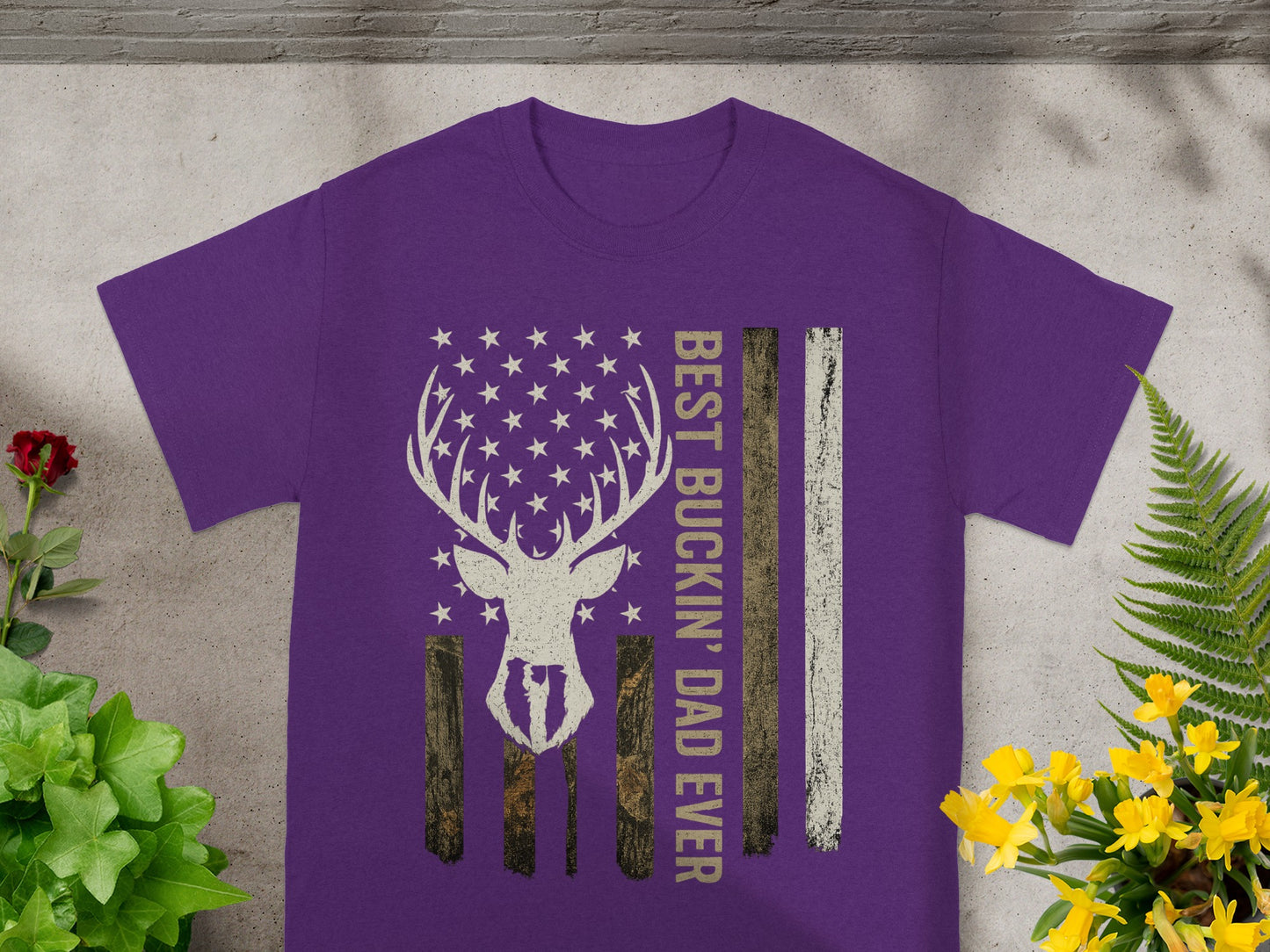 Purple t-shirt with deer silhouette, stars, wood grain, and text "BEST BUCKIN' DAD EVER".