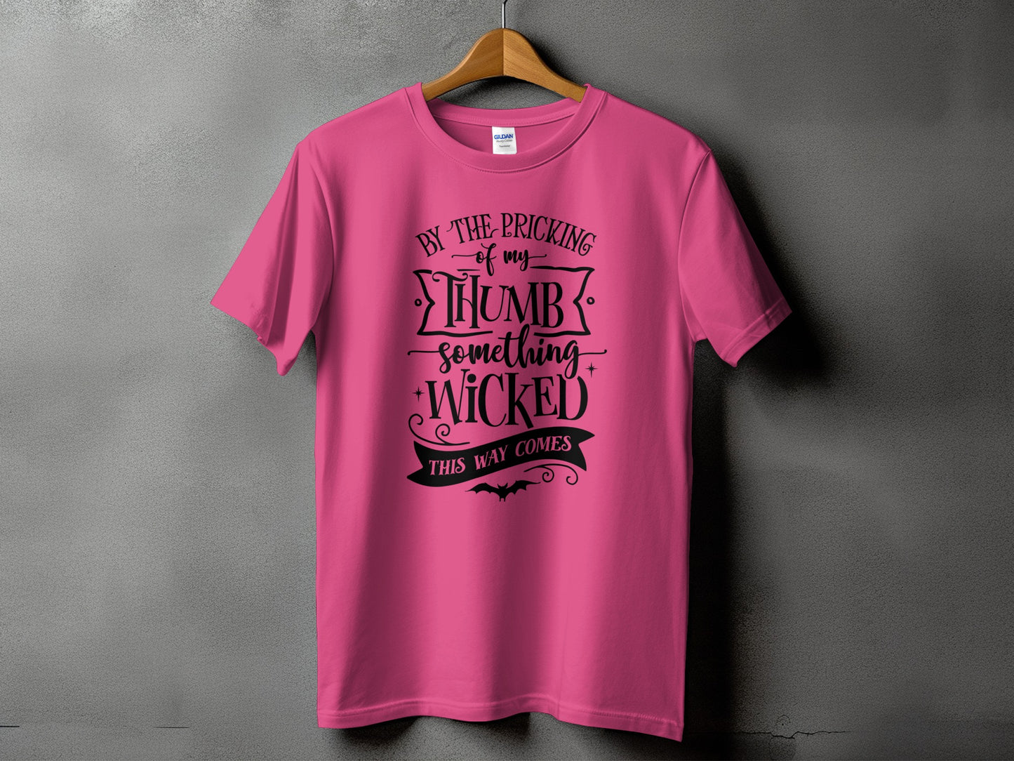 Pink t-shirt with black text reading "BY THE PRICKING of my THUMB something WICKED THIS WAY COMES".