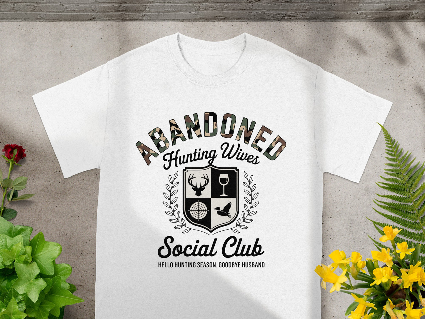 White t-shirt with "Abandoned Hunting Wives Social Club" text and shield graphic.