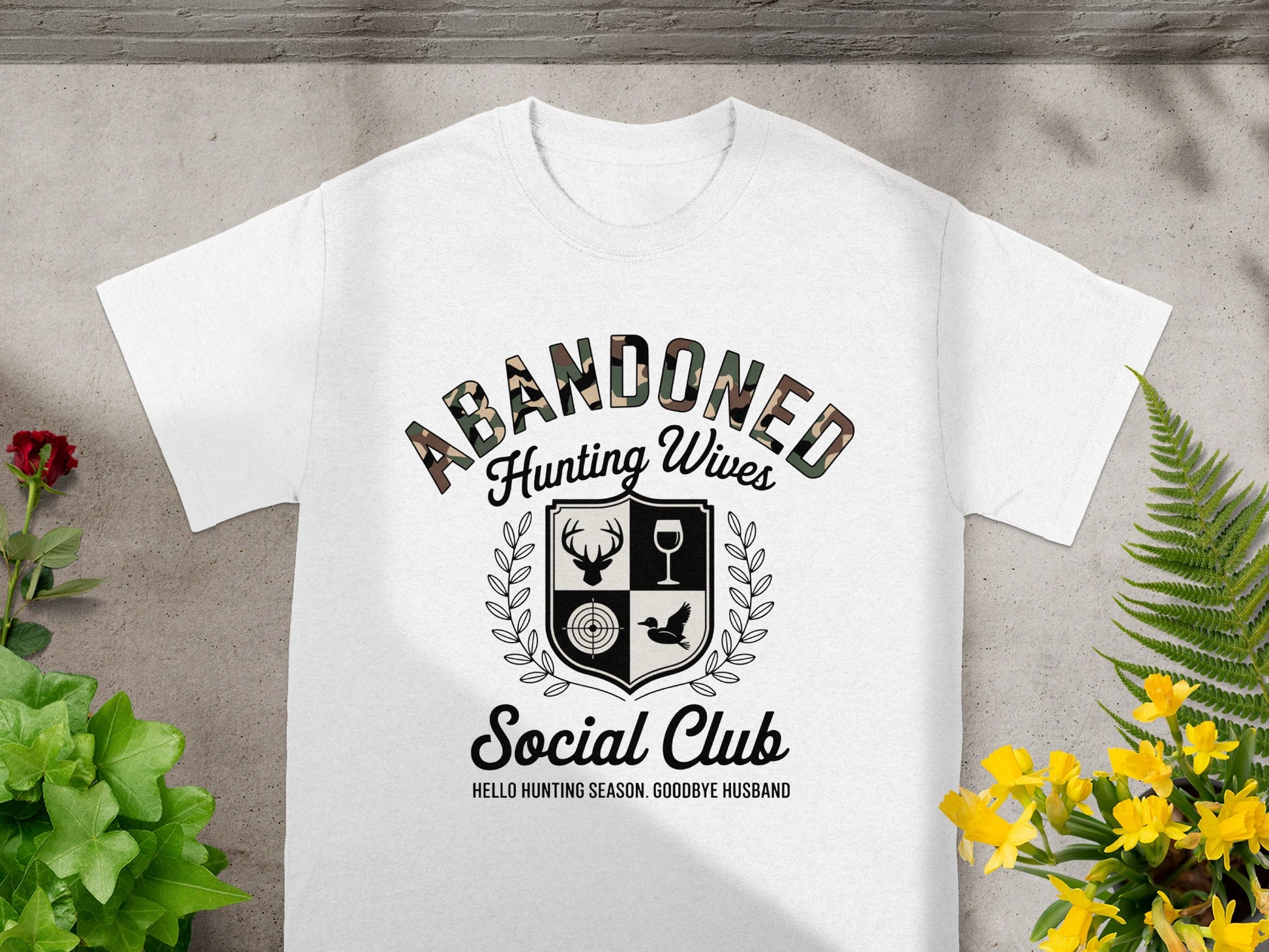 White t-shirt with "Abandoned Hunting Wives Social Club" text and shield graphic.