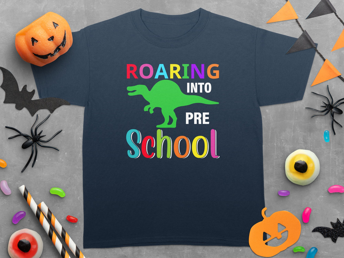 Dinosaur graphic tee with "ROARING INTO PRE SCHOOL" text, surrounded by Halloween decorations.