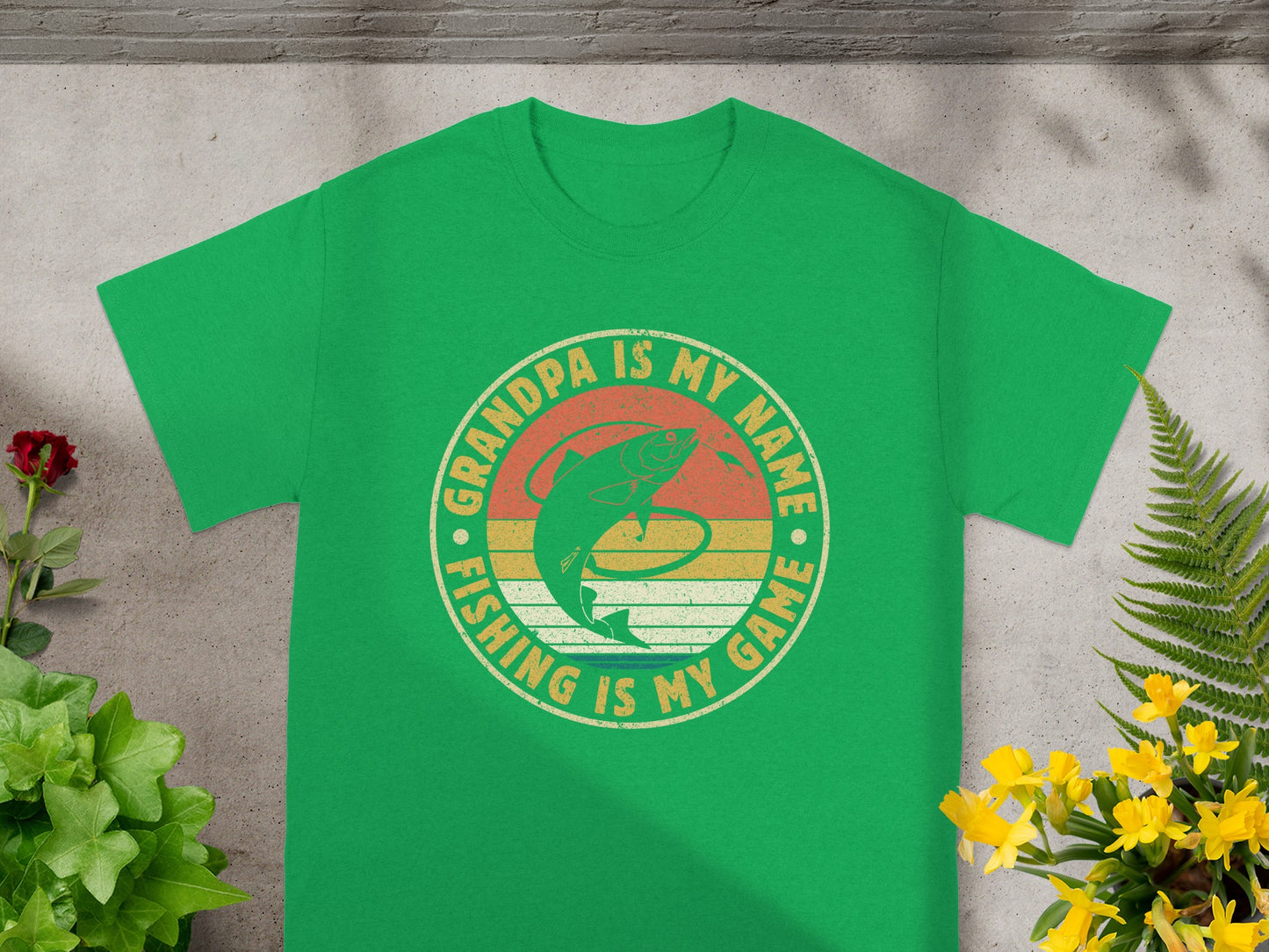 Green t-shirt graphic with a fish and text: Grandpa is my name, fishing is my game.
