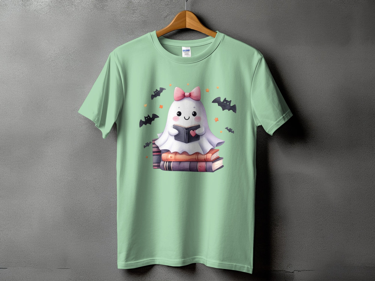Cute ghost reading a book, surrounded by bats and stars, on a light green t-shirt.