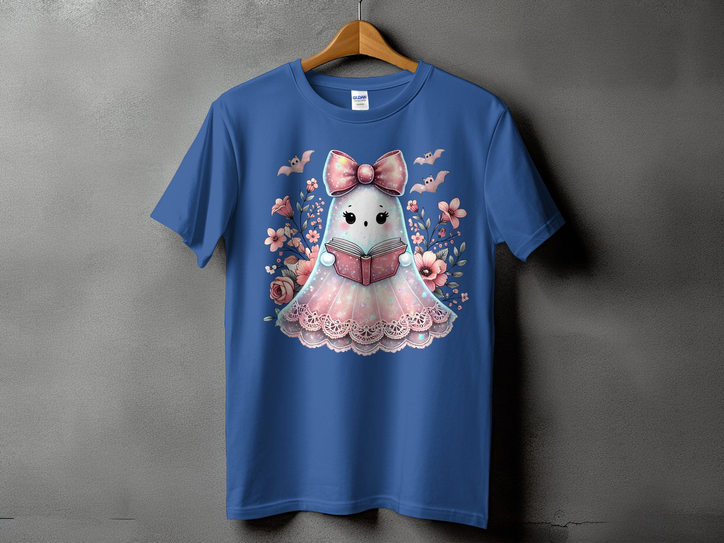 Blue t-shirt with a cute ghost reading a book surrounded by flowers and bats.