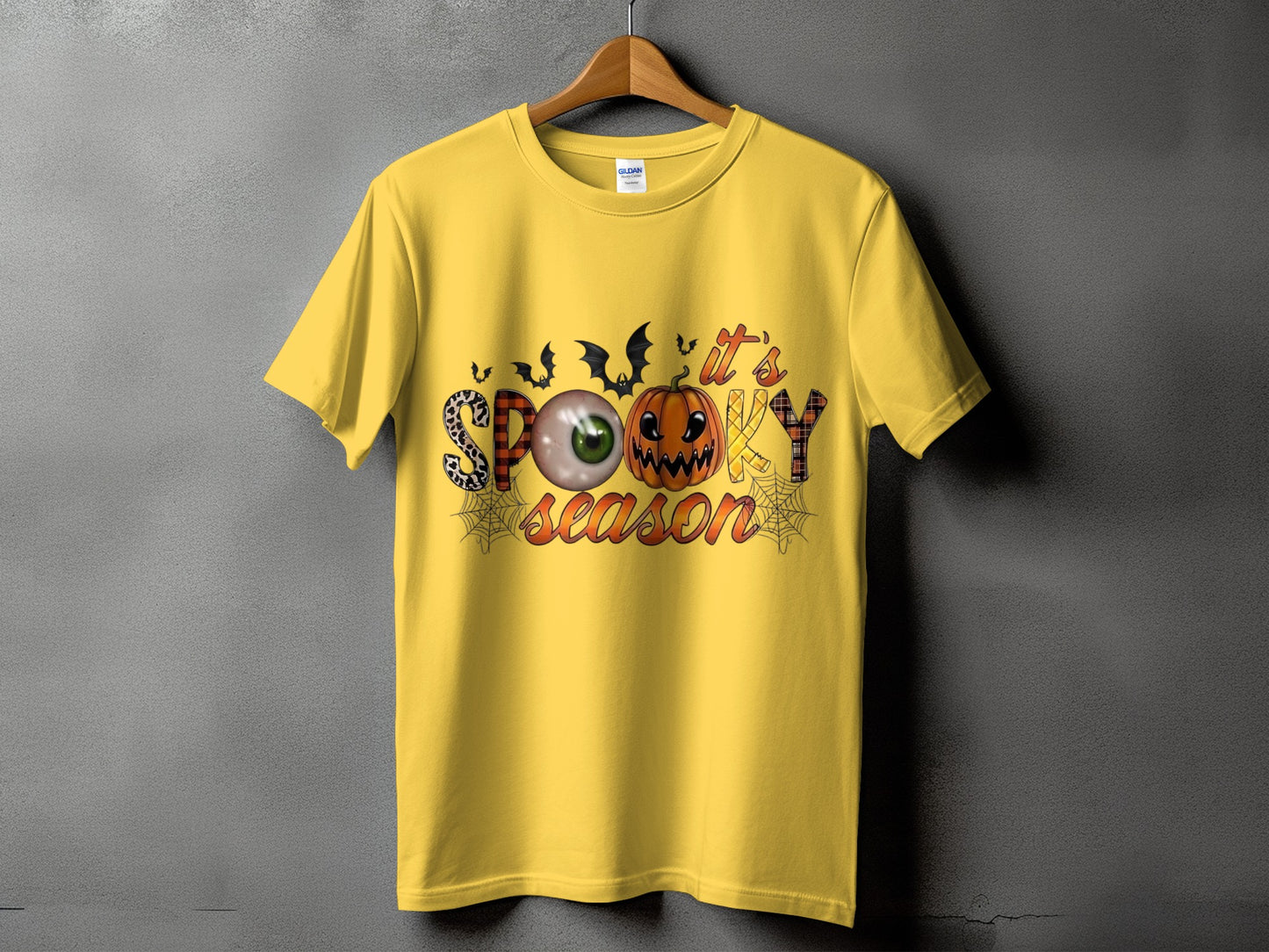 Yellow t-shirt with "it's spooky season" Halloween graphic featuring bats and pumpkin.