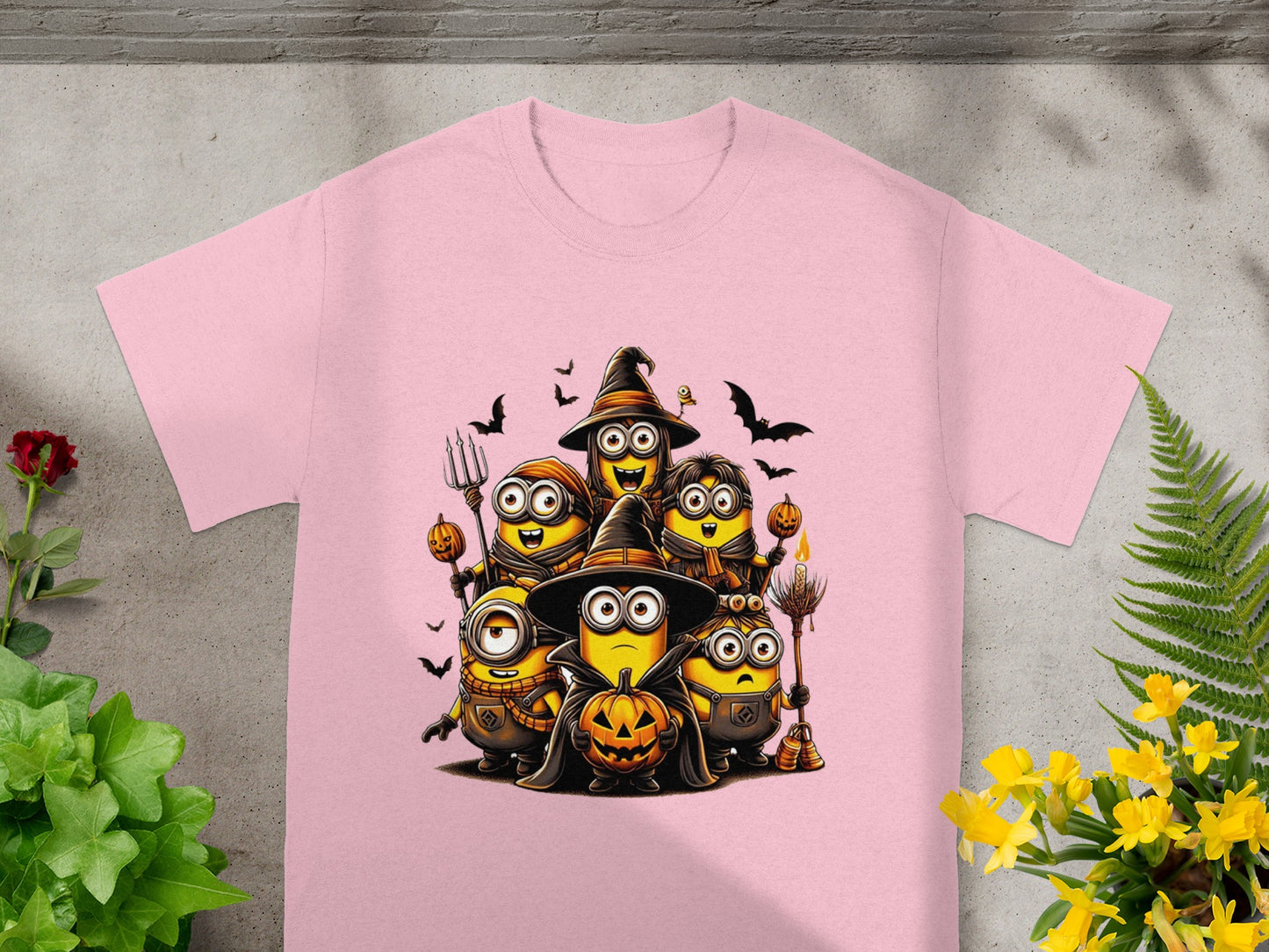 Minions in Halloween costumes holding pumpkins and brooms on a pink t-shirt.