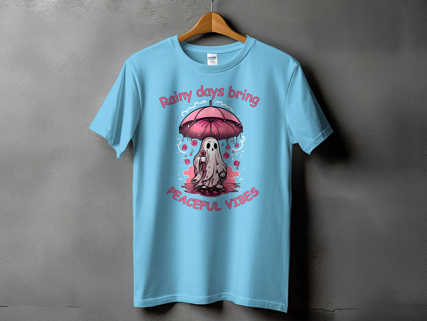 Light blue t-shirt with ghost under umbrella and text "Rainy days bring peaceful vibes".