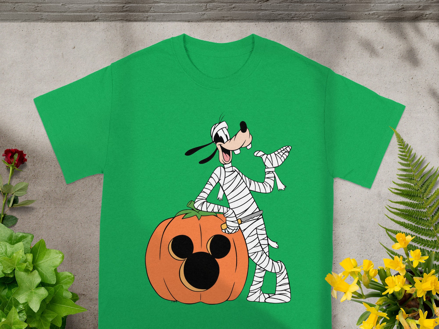 Mummy Goofy poses with a Mickey Mouse jack-o'-lantern on a green t-shirt.