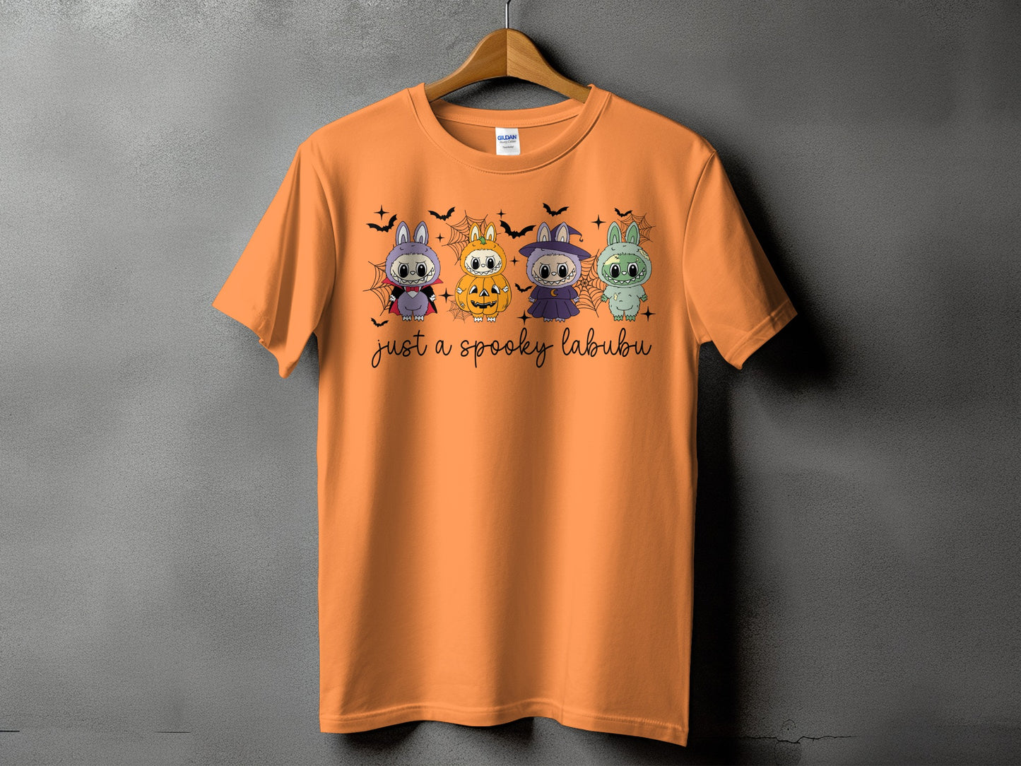 Orange t-shirt with four cute characters in Halloween costumes and text "just a spooky labubu".