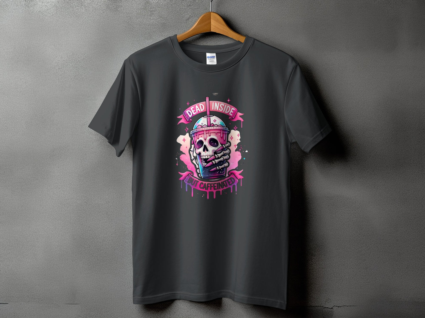 Dark gray t-shirt featuring a skull holding a pink drink with text "DEAD INSIDE BUT CAFFEINATED".