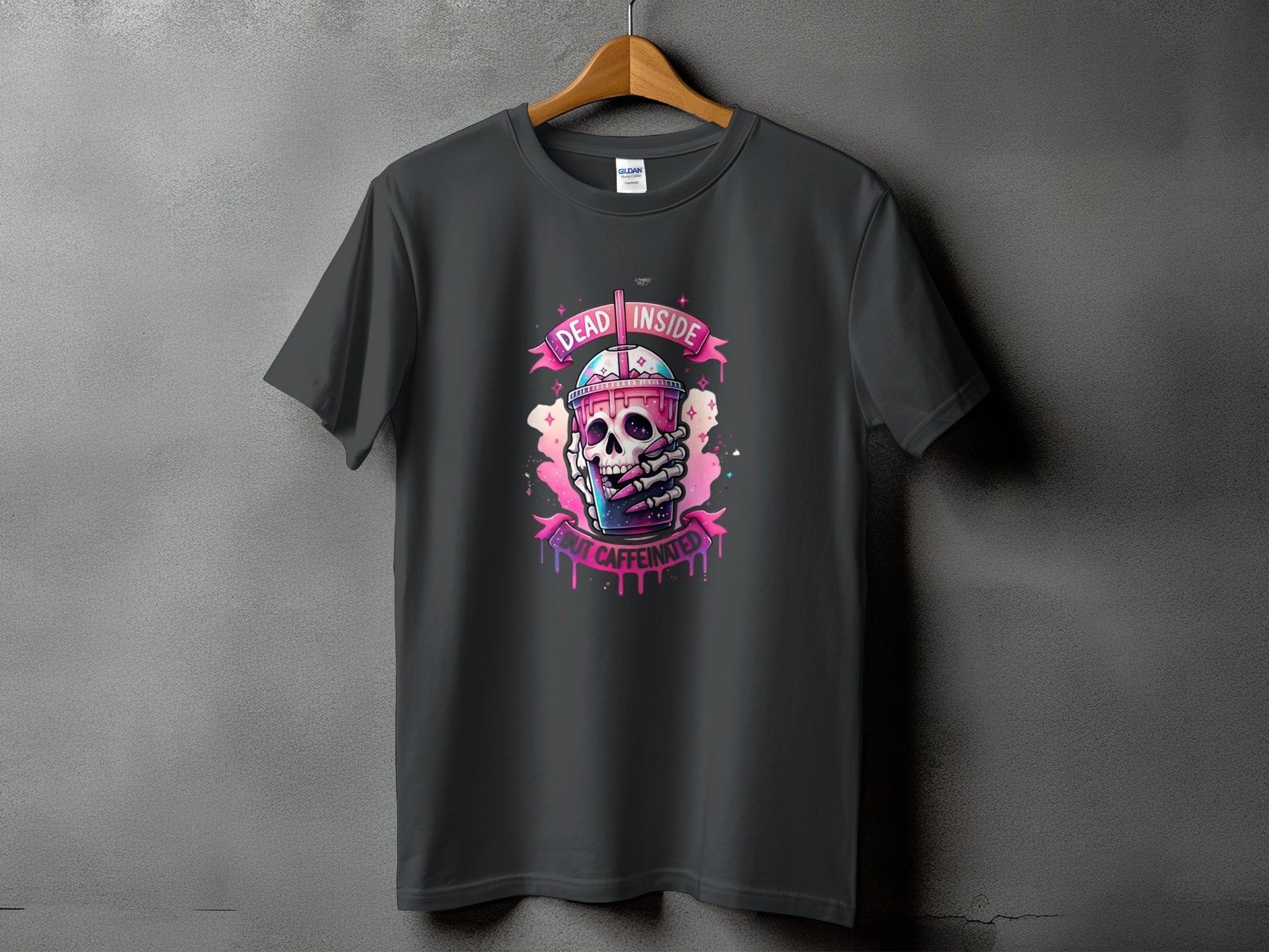 Dark gray t-shirt featuring a skull holding a pink drink with text "DEAD INSIDE BUT CAFFEINATED".