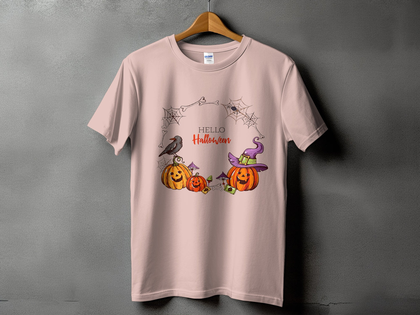 Pink t-shirt with "Hello Halloween" text surrounded by pumpkins, a crow, and cobwebs.