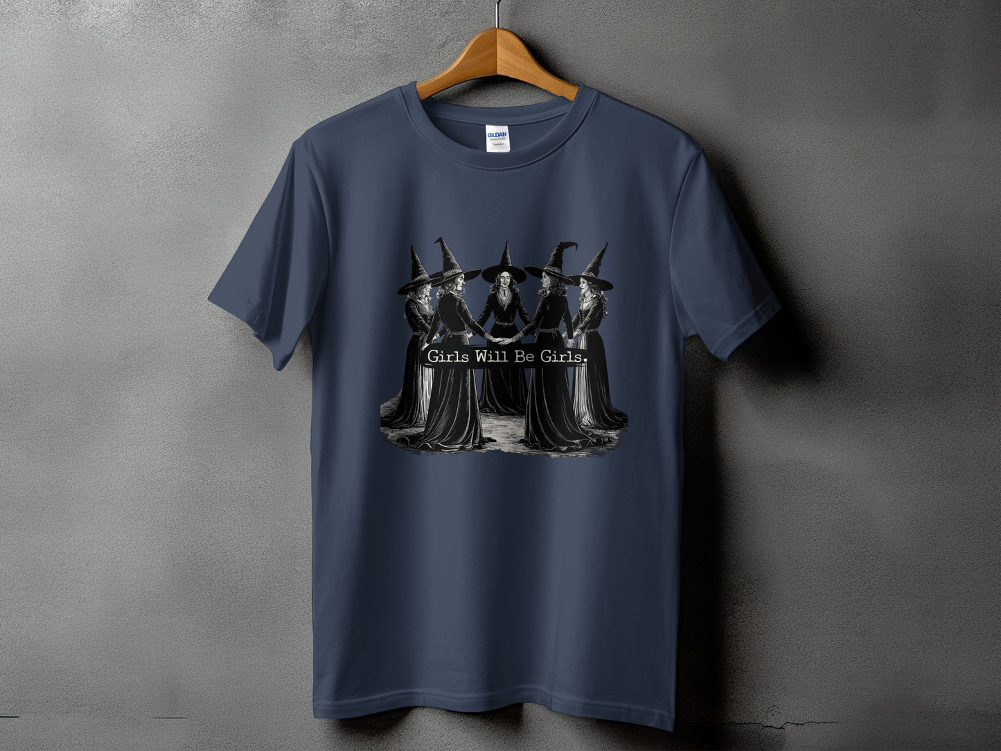 Dark blue t-shirt with five witches in a circle, text reads "Girls Will Be Girls."
