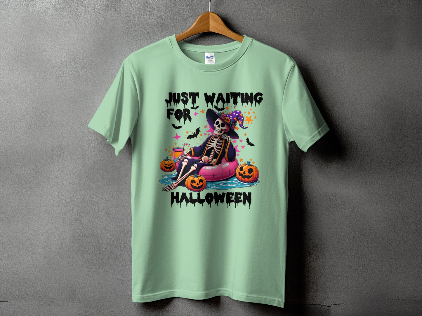 Light green t-shirt with skeleton on float, pumpkins, and text "Just Waiting For Halloween."