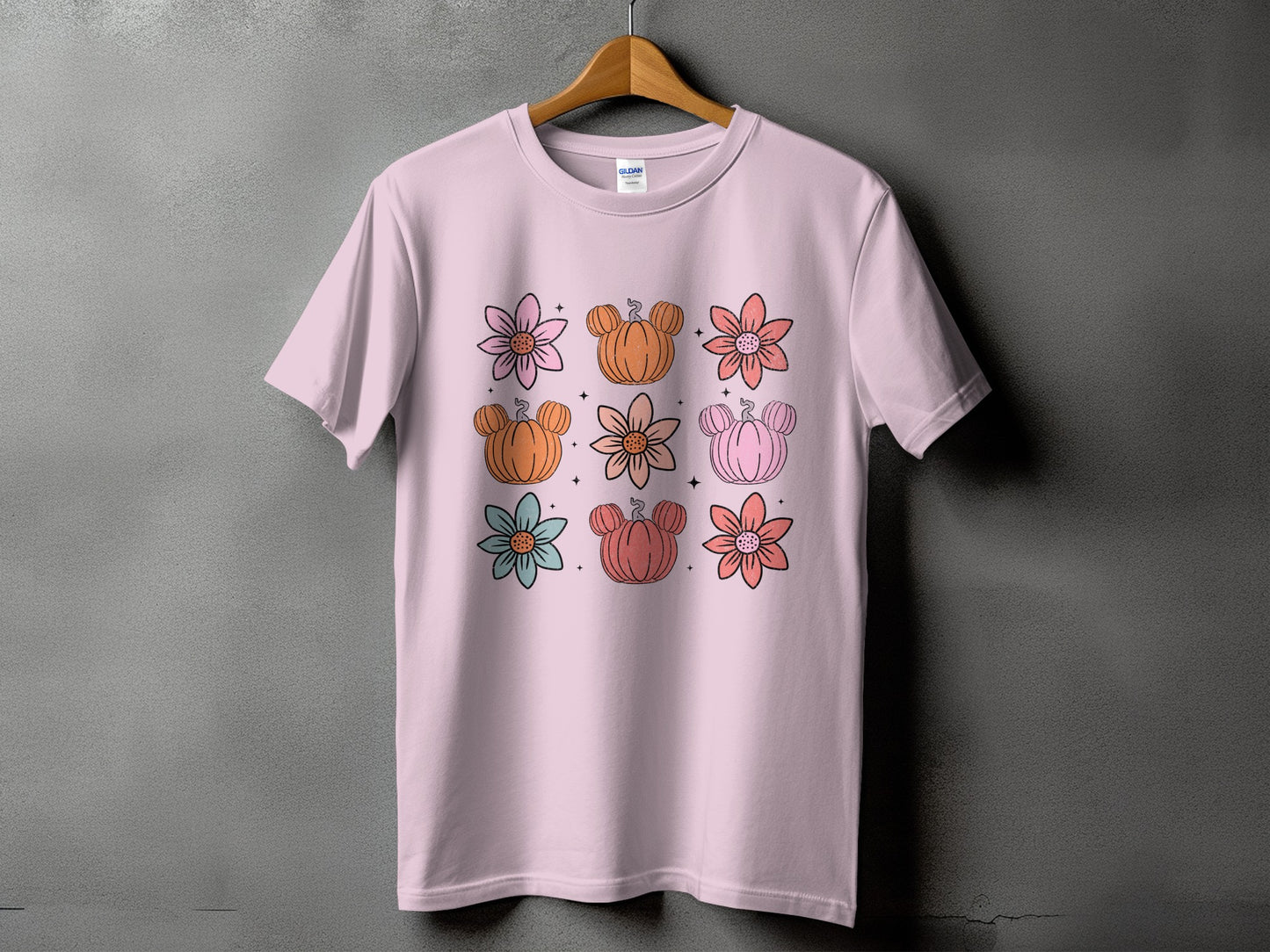 Pink t-shirt with a grid of nine illustrations featuring flowers and Mickey Mouse-shaped pumpkins.