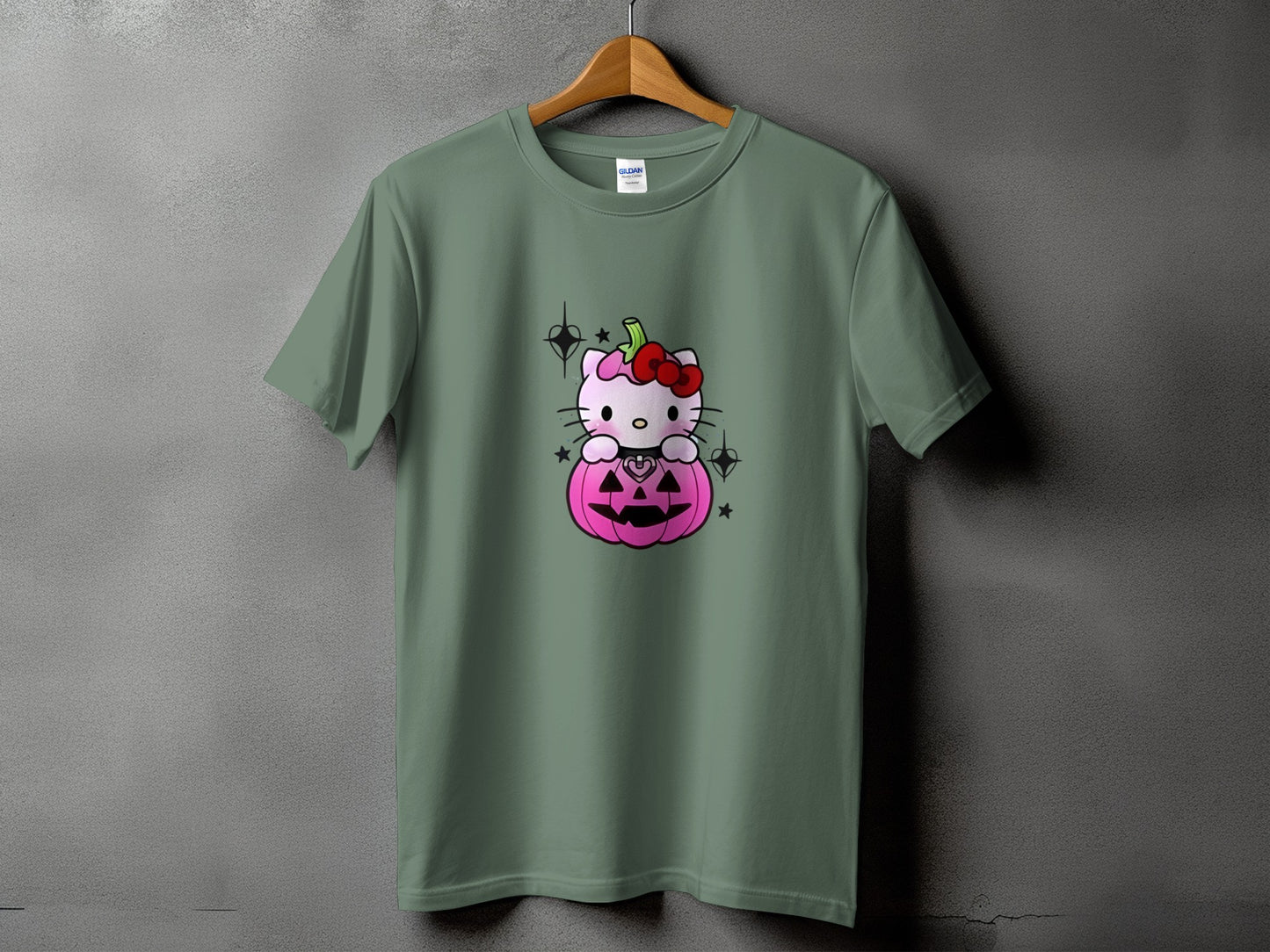 Hello Kitty sits on a pink pumpkin with a red bow, on a green t-shirt.